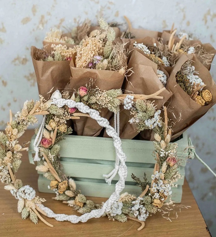 Mit Trockenblumen und hellem Garn geschmückte Ringe vor kleinen Blumensträußen in braunem Papier