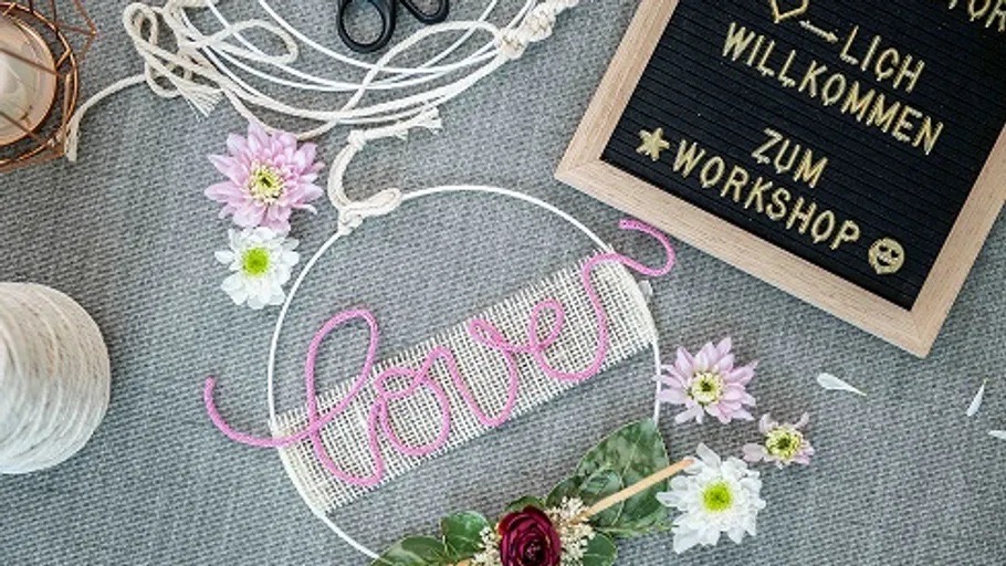 Ein mit Blüten geschmückter Metallring mit dem Schriftzug love aus rosa Garn