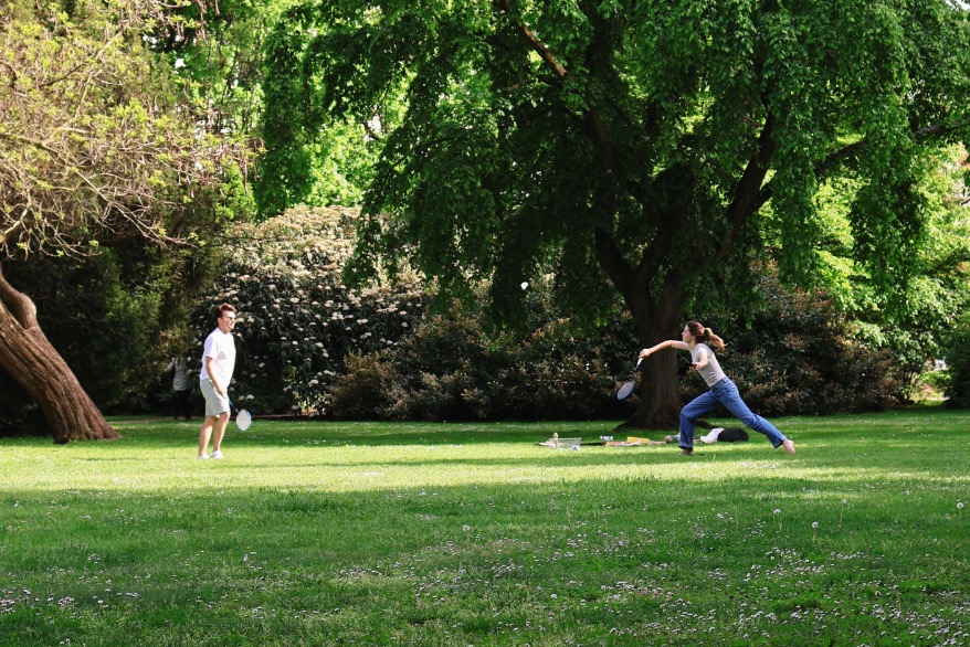 Zwei Menschen spielen gemeinsam Badminton in einem grünen Park
